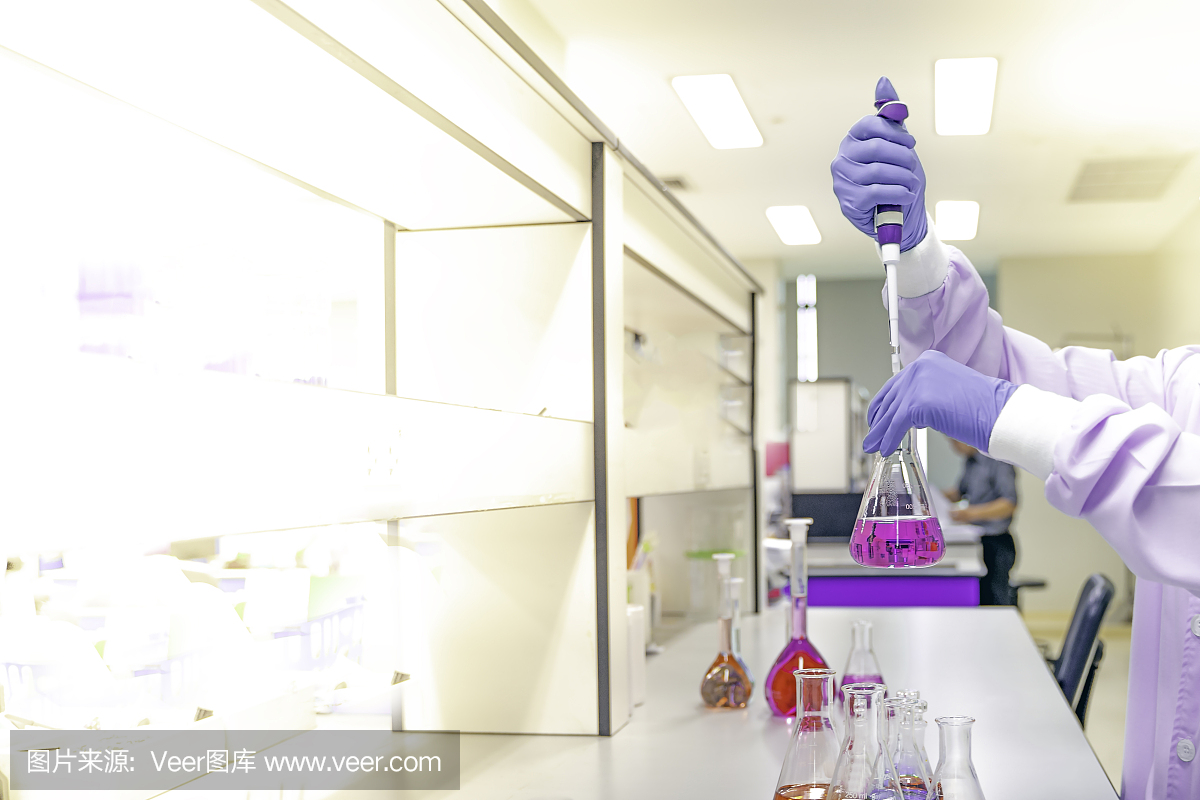 科学家双手戴上紫色橡胶手套,在科学实验室里用含有各种化学物质的玻璃瓶进行研发理念的实验。浅聚焦效果。